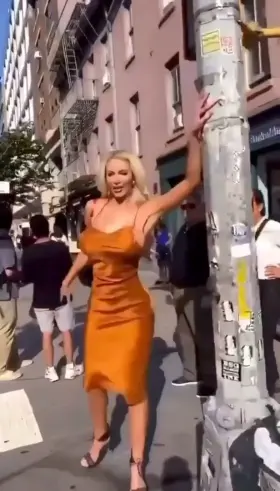 Who is the woman in this video? Description: blonde woman with large implants wearing orange cowl neck dress dancing & flashing on NYC street/crosswalks, grinding on cop car, to a remix of 